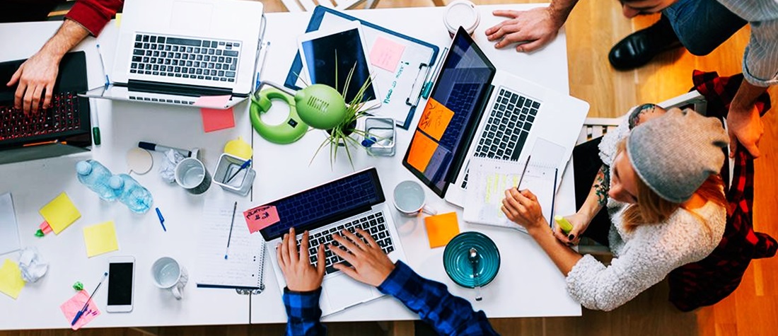 En una mesa de juntas con varias computadoras, compañeros de trabajo planifican 