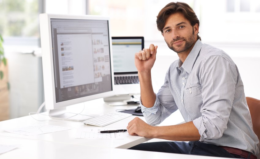 Un hombre frente a su computadora, sonrié a cámara