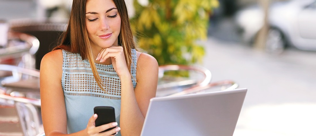 Una mujer ve su celular sentada frente a una computadora